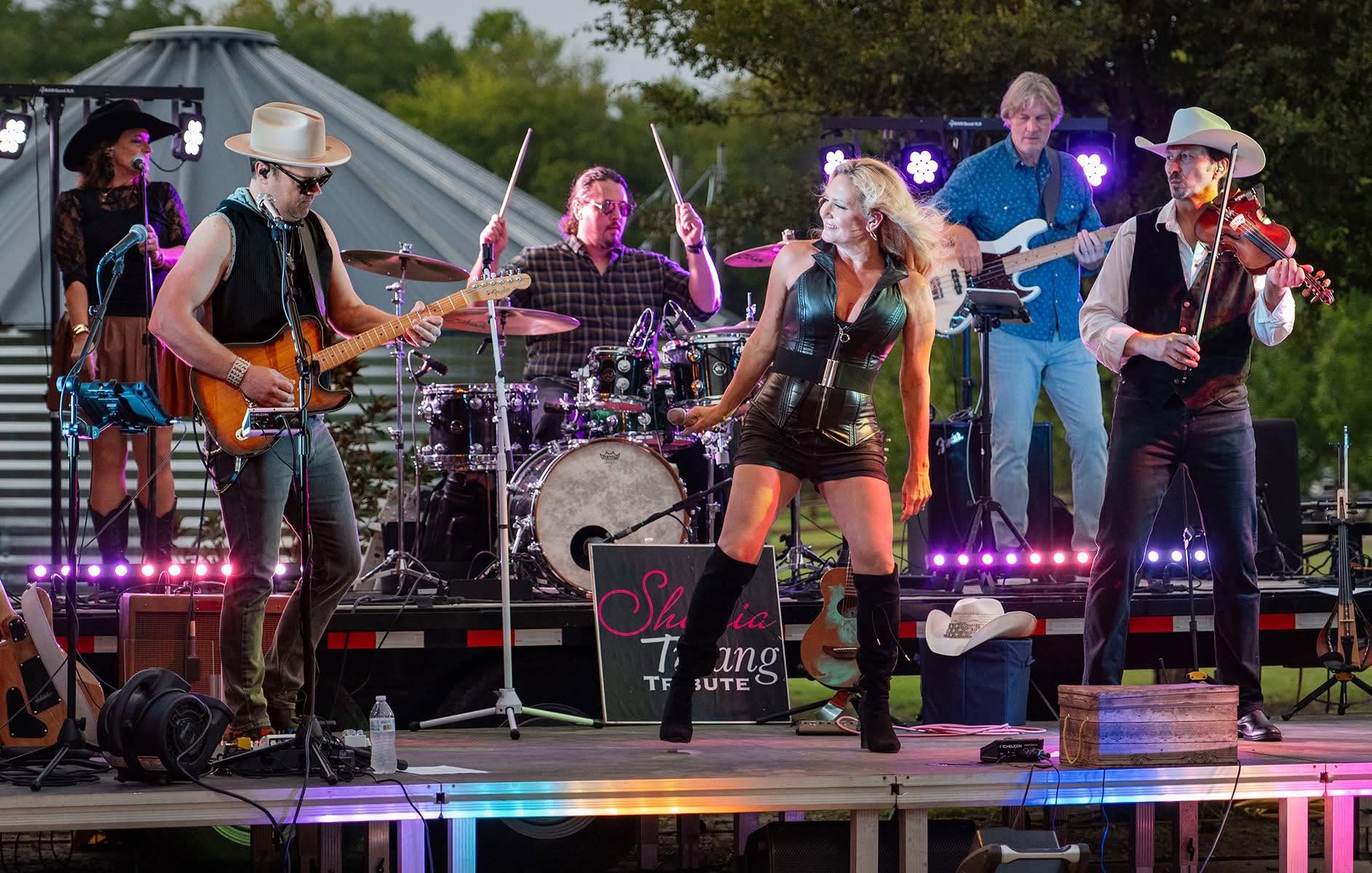 Shania Twang performing outdoors with a full band.