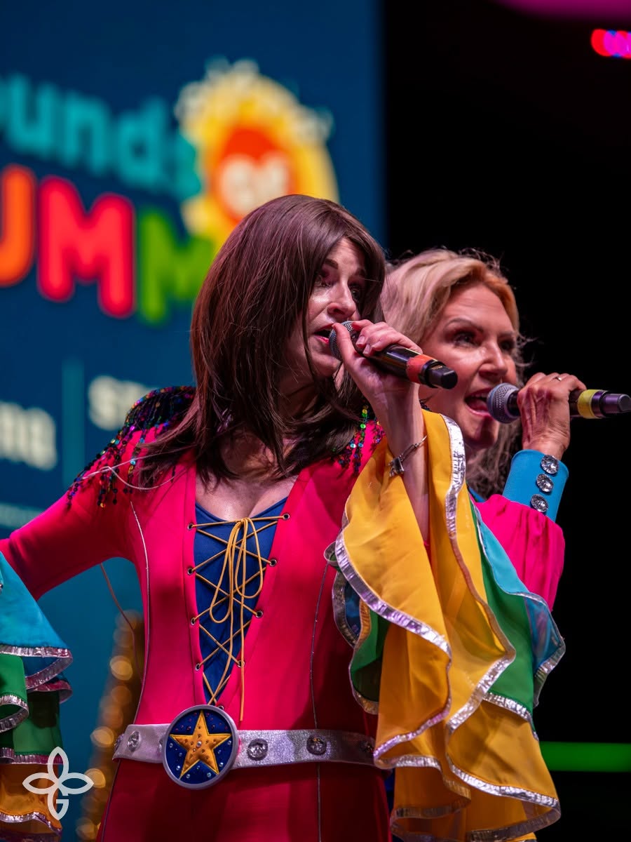 Two Super Trouper singers in colorful ABBA-inspired costumes under stage lights.
