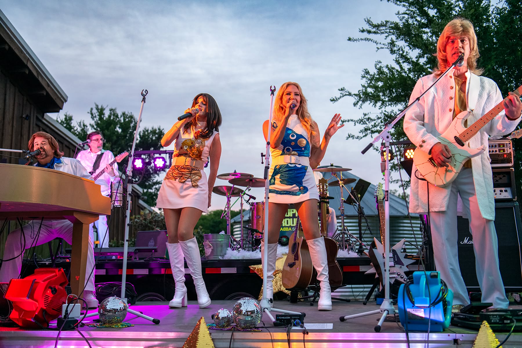 Super Trouper performers in ABBA-inspired costumes on an outdoor stage.