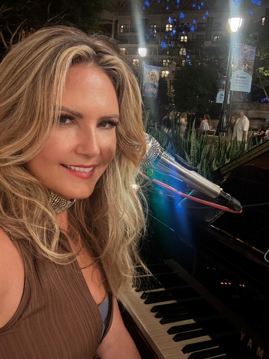 Dālene Richelle smiling beside a piano and microphone during an evening performance.